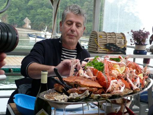 Anthony Bourdain sampling a food platter on his travels. (Photo Source: The Travel Channel)